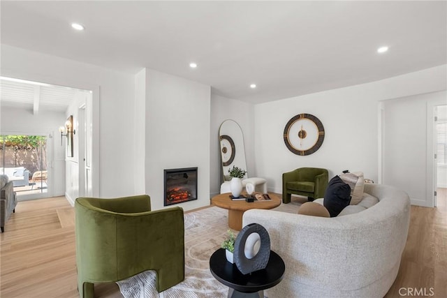 living room featuring recessed lighting, light wood-style flooring, a glass covered fireplace, and beamed ceiling