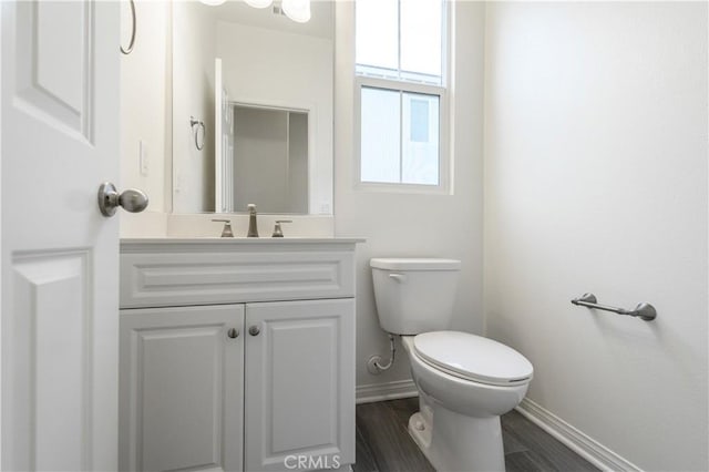 bathroom with toilet, wood finished floors, vanity, and baseboards