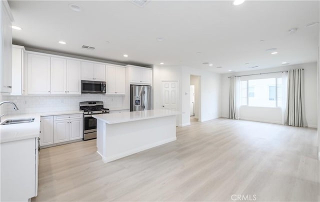 kitchen with a center island, a sink, light wood-type flooring, appliances with stainless steel finishes, and decorative backsplash