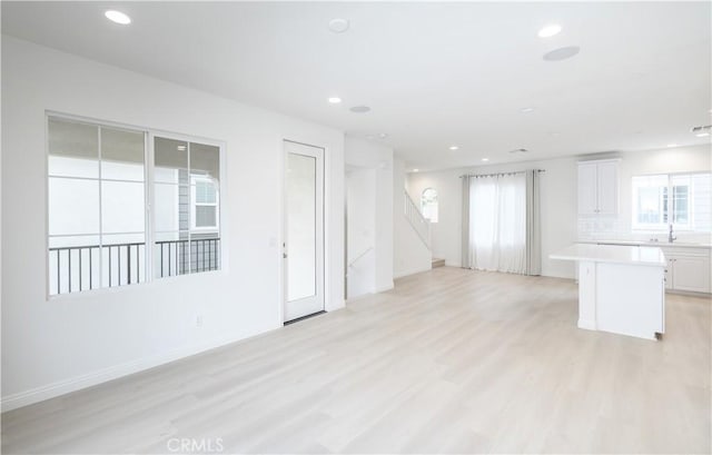 unfurnished living room featuring recessed lighting, stairs, light wood-type flooring, and baseboards