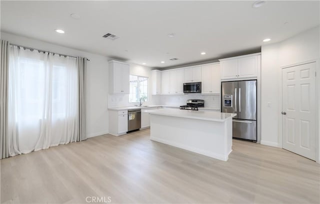 kitchen featuring light wood-style flooring, white cabinets, visible vents, stainless steel appliances, and decorative backsplash