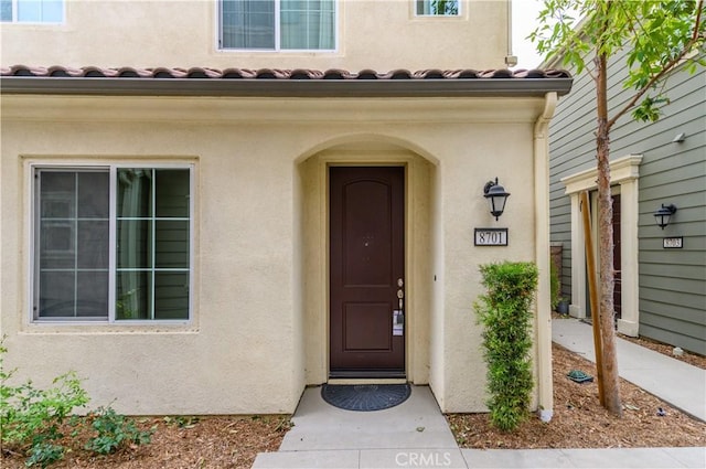 view of exterior entry with stucco siding and a tiled roof
