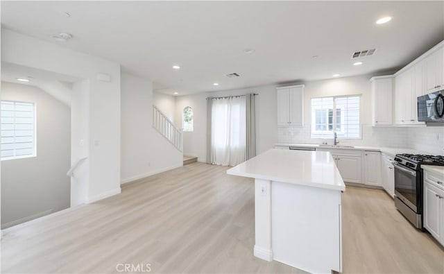 kitchen with gas range oven, a center island, light wood-style floors, visible vents, and a sink