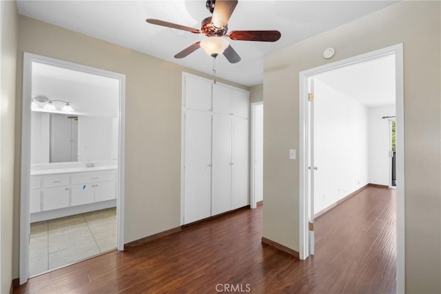 unfurnished bedroom featuring dark wood-type flooring, a closet, ensuite bath, a sink, and baseboards