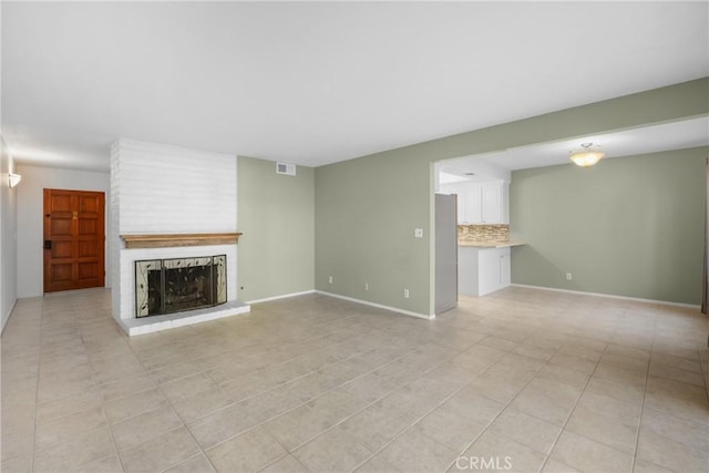 unfurnished living room with baseboards, light tile patterned floors, a brick fireplace, and visible vents
