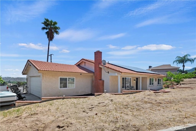 15160 Darnell Dr, Lake Elsinore, CA 92530 - rear view of property featuring a tile roof, stucco siding, a chimney, an attached garage, and roof mounted solar panels