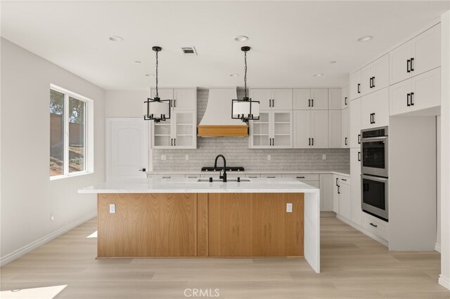 5978 Copperfield Ave, Riverside, CA 92506 - kitchen featuring custom range hood, double oven, a kitchen island with sink, light wood finished floors, and recessed lighting
