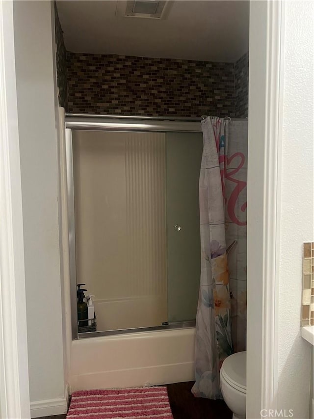 bathroom featuring shower / bath combination with glass door, toilet, and visible vents
