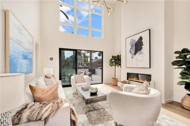 607 12th St, Huntington Beach, CA 92648 - living area featuring a glass covered fireplace, a towering ceiling, baseboards, a chandelier, and wood finished floors