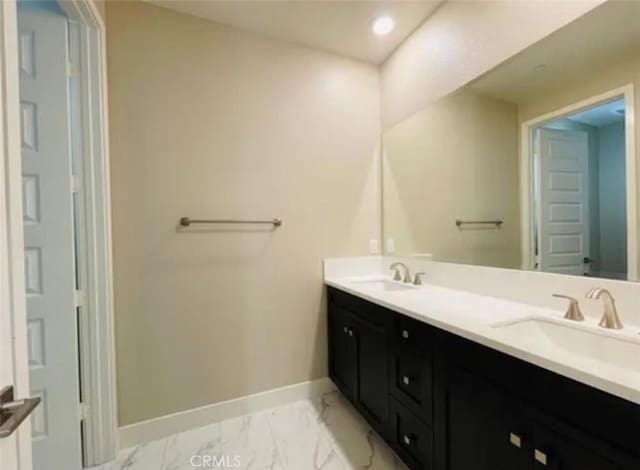 full bath featuring double vanity, marble finish floor, a sink, and baseboards
