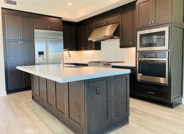 kitchen with a sink, visible vents, light wood-style floors, and under cabinet range hood