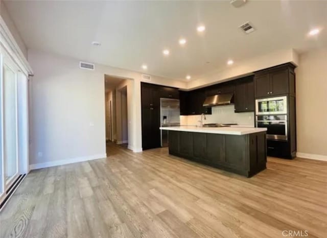 kitchen featuring visible vents, light countertops, light wood-type flooring, under cabinet range hood, and stainless steel appliances