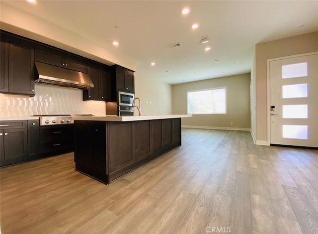 kitchen with visible vents, under cabinet range hood, a kitchen island with sink, light countertops, and appliances with stainless steel finishes