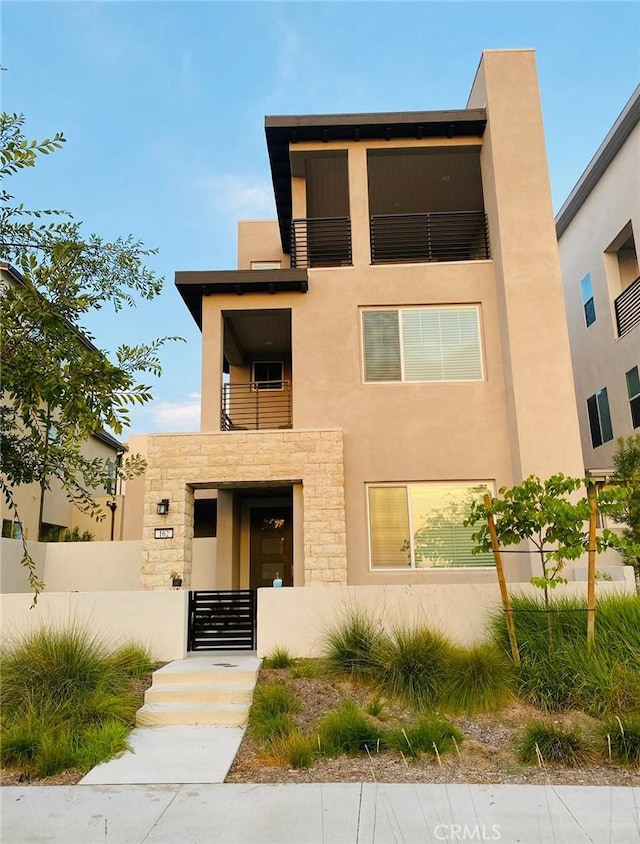 contemporary home featuring a fenced front yard, stucco siding, stone siding, and a balcony