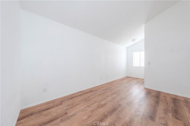 spare room featuring baseboards, light wood-style flooring, and lofted ceiling