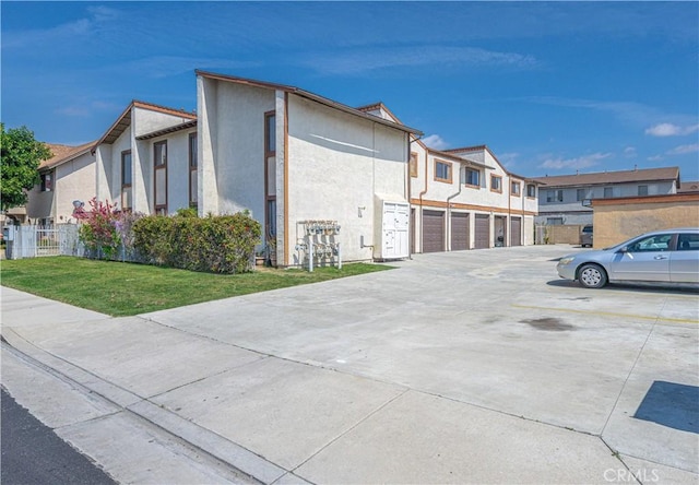 view of side of property with stucco siding, concrete driveway, an attached garage, a yard, and a residential view