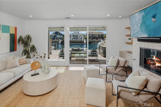 living area featuring crown molding, a textured ceiling, a stone fireplace, and a wealth of natural light