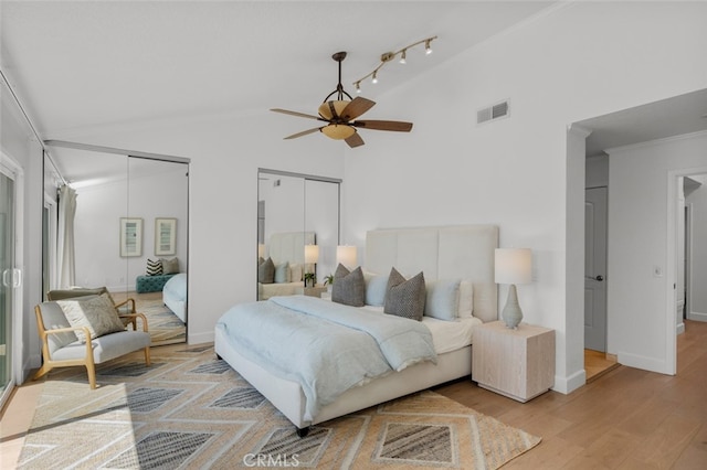 bedroom with baseboards, light wood-type flooring, crown molding, visible vents, and multiple closets