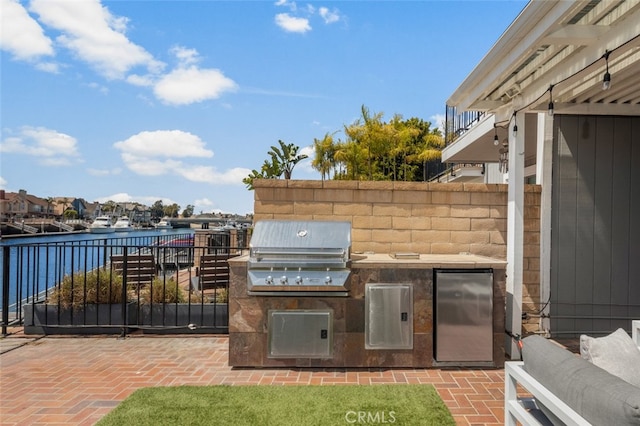 view of patio / terrace with a water view, fence, area for grilling, and an outdoor kitchen