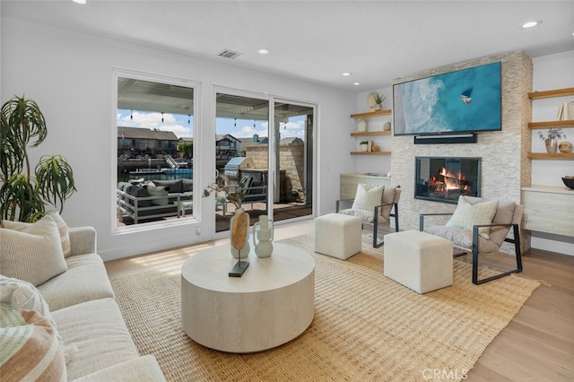 living area with visible vents, a stone fireplace, recessed lighting, and wood finished floors