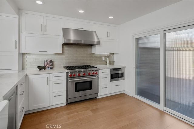 kitchen featuring tasteful backsplash, white cabinetry, exhaust hood, appliances with stainless steel finishes, and light wood finished floors