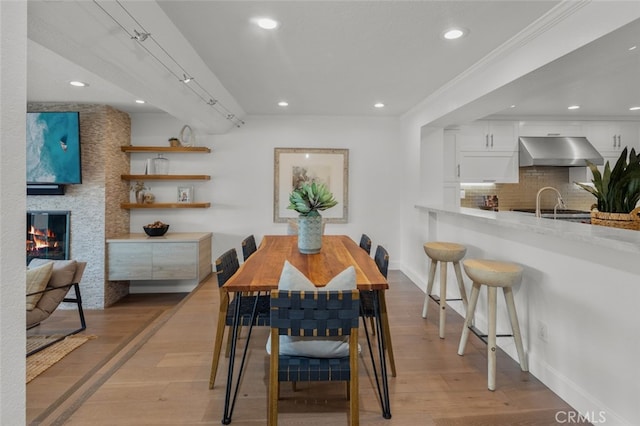 dining room with ornamental molding, a large fireplace, recessed lighting, light wood finished floors, and baseboards