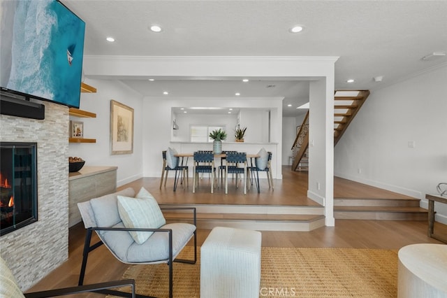living room featuring a stone fireplace, baseboards, recessed lighting, stairs, and wood finished floors