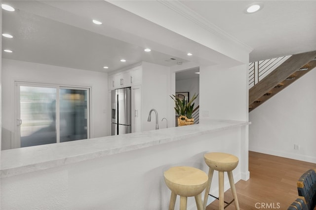 kitchen with stainless steel fridge with ice dispenser, baseboards, white cabinets, light wood finished floors, and recessed lighting