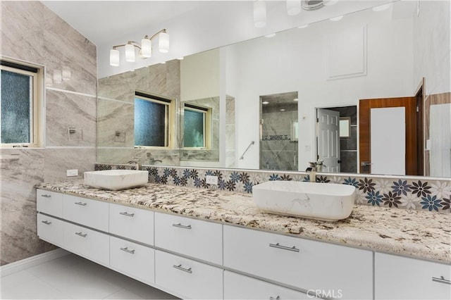 bathroom featuring a shower stall, double vanity, a sink, and tile walls