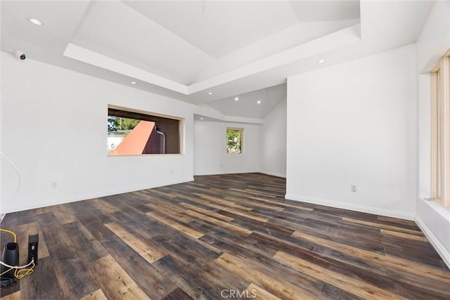 empty room with baseboards, vaulted ceiling, recessed lighting, a tray ceiling, and wood finished floors