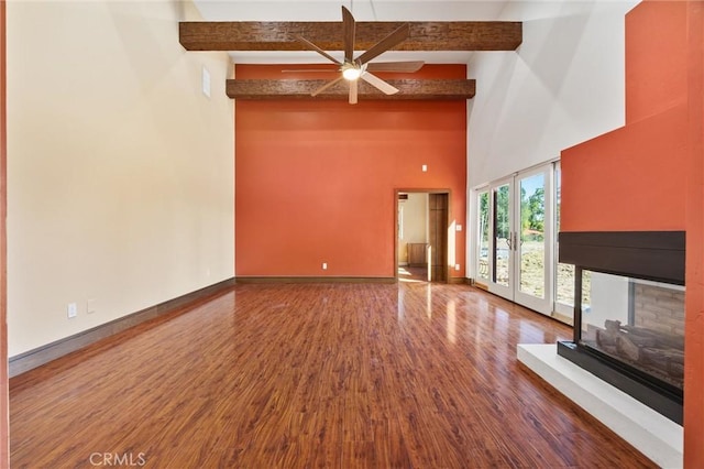 unfurnished living room featuring wood finished floors, ceiling fan, baseboards, and beamed ceiling