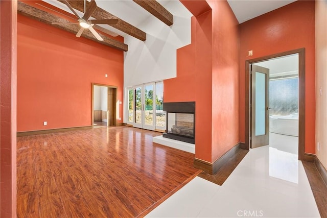unfurnished living room featuring baseboards, a multi sided fireplace, ceiling fan, beamed ceiling, and high vaulted ceiling