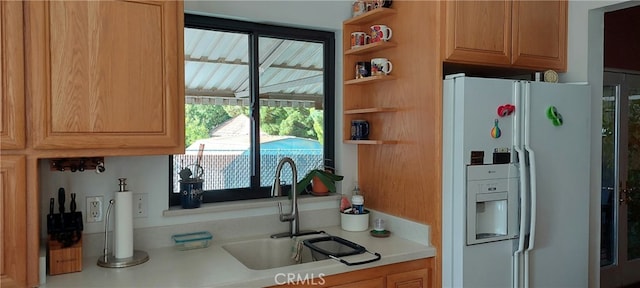 kitchen with a sink, open shelves, white fridge with ice dispenser, and light countertops