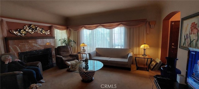 carpeted living room featuring a high end fireplace and arched walkways