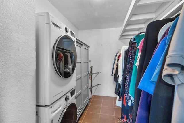 clothes washing area with stacked washer / drying machine, dark tile patterned floors, and laundry area