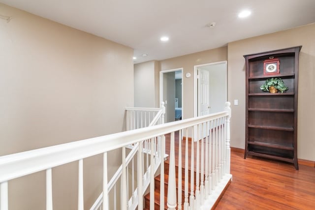 hallway with wood finished floors, baseboards, an upstairs landing, and recessed lighting