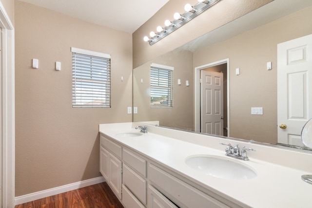 bathroom with a sink, baseboards, double vanity, and wood finished floors