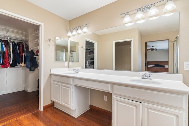 bathroom featuring a sink, a spacious closet, double vanity, and wood finished floors