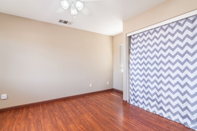 empty room with baseboards, a ceiling fan, dark wood-type flooring, visible vents, and an accent wall
