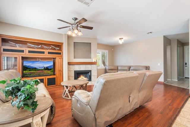 living area featuring a fireplace, visible vents, a ceiling fan, and wood finished floors