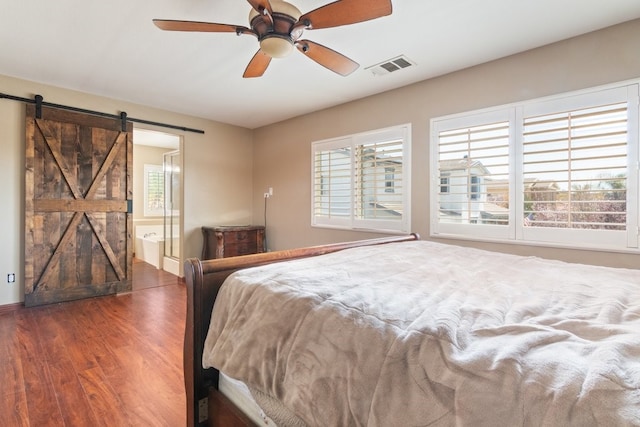 bedroom with connected bathroom, a barn door, visible vents, ceiling fan, and wood finished floors