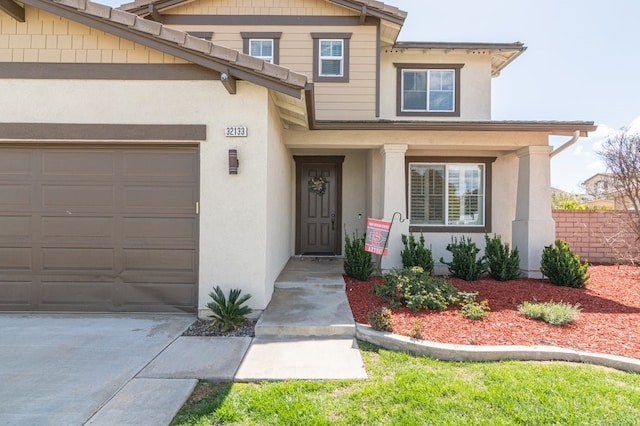 doorway to property with an attached garage, driveway, and stucco siding