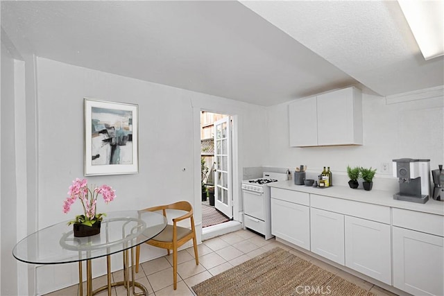 kitchen featuring white range with gas cooktop, light countertops, white cabinets, and light tile patterned flooring