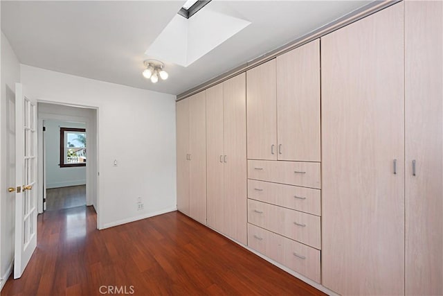 unfurnished bedroom featuring a skylight, baseboards, dark wood-style floors, and a closet