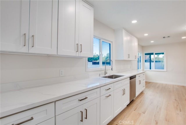 kitchen featuring stainless steel dishwasher, white cabinetry, light stone counters, a sink, and light wood finished floors