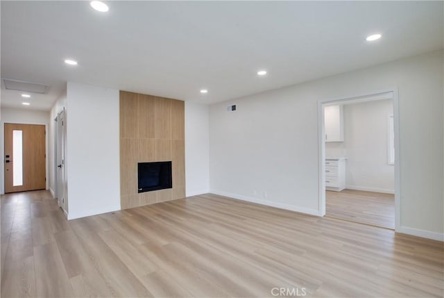 unfurnished living room featuring light wood-type flooring, baseboards, a large fireplace, and recessed lighting