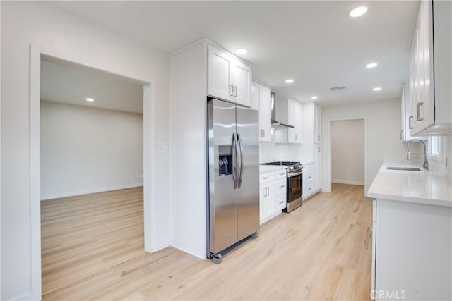 kitchen featuring light wood-type flooring, wall chimney range hood, light countertops, a sink, and stainless steel appliances