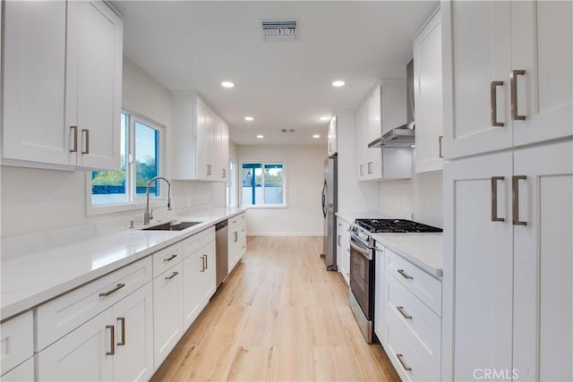 kitchen with light wood-style floors, white cabinets, a sink, stainless steel appliances, and baseboards