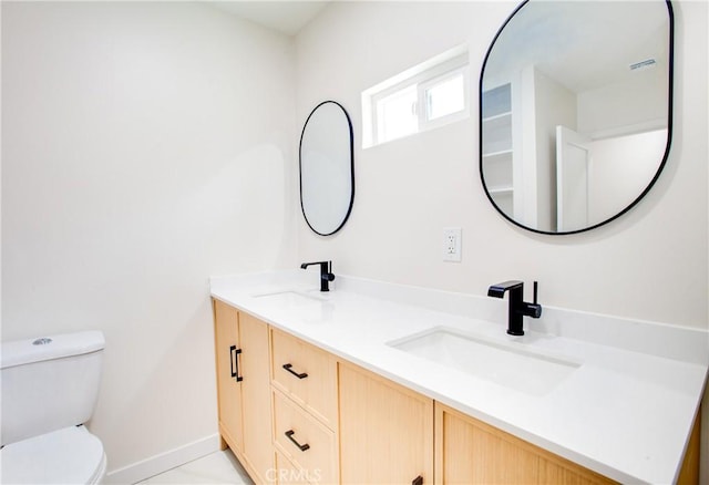 bathroom featuring double vanity, baseboards, a sink, and toilet