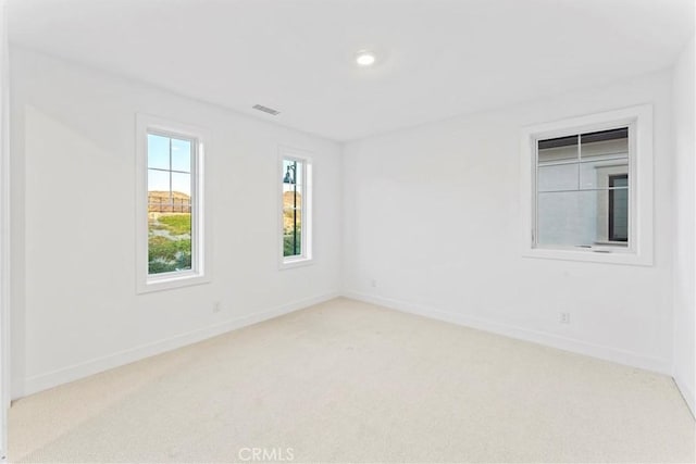 empty room featuring visible vents, light colored carpet, and baseboards